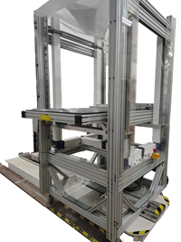 Silver multi-level automated industrial machine handling white material. Yellow and black safety stripes on the base.
