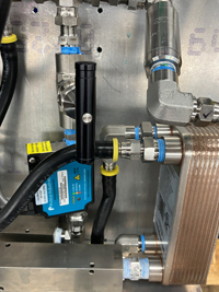 Close-up of stainless steel pipes, blue-banded connectors, and a blue sensor with black tubing in a complex system.