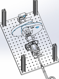 CAD rendering of a mechanical assembly on a perforated silver plate. Features a central rotating platform and extending arm.