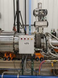 Large metallic pipe system on orange supports with a white 'UZG' control box, red/yellow indicator lights, and blue pipes.