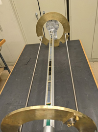 Scientific instrument with two large, curved brass plates, a central metallic rectangular bar, on a dark lab bench.